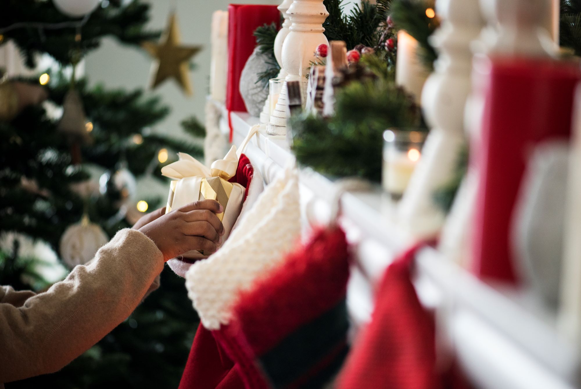 Person putting wrapped gift into stocking on mantle